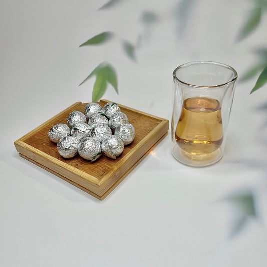 Silver wrapped items on a wooden coaster with a glass of tea.